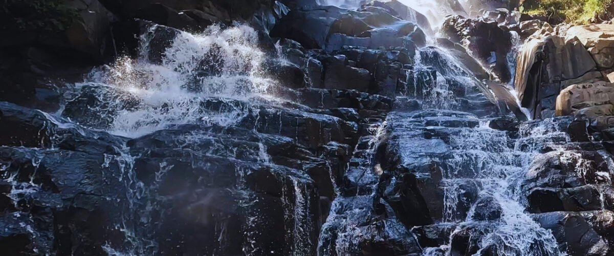 Waterfall cascading over dark rock into a tea coloured rock pool on the Lynx Loop at Wathaba Hiking Trails, Mpumalanga