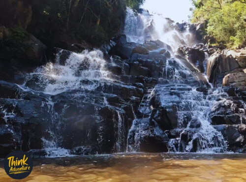 Waterfall cascading over dark rock into a tea-coloured rock pool on the Lynx Loop at Wathaba Hiking Trails, Mpumalanga