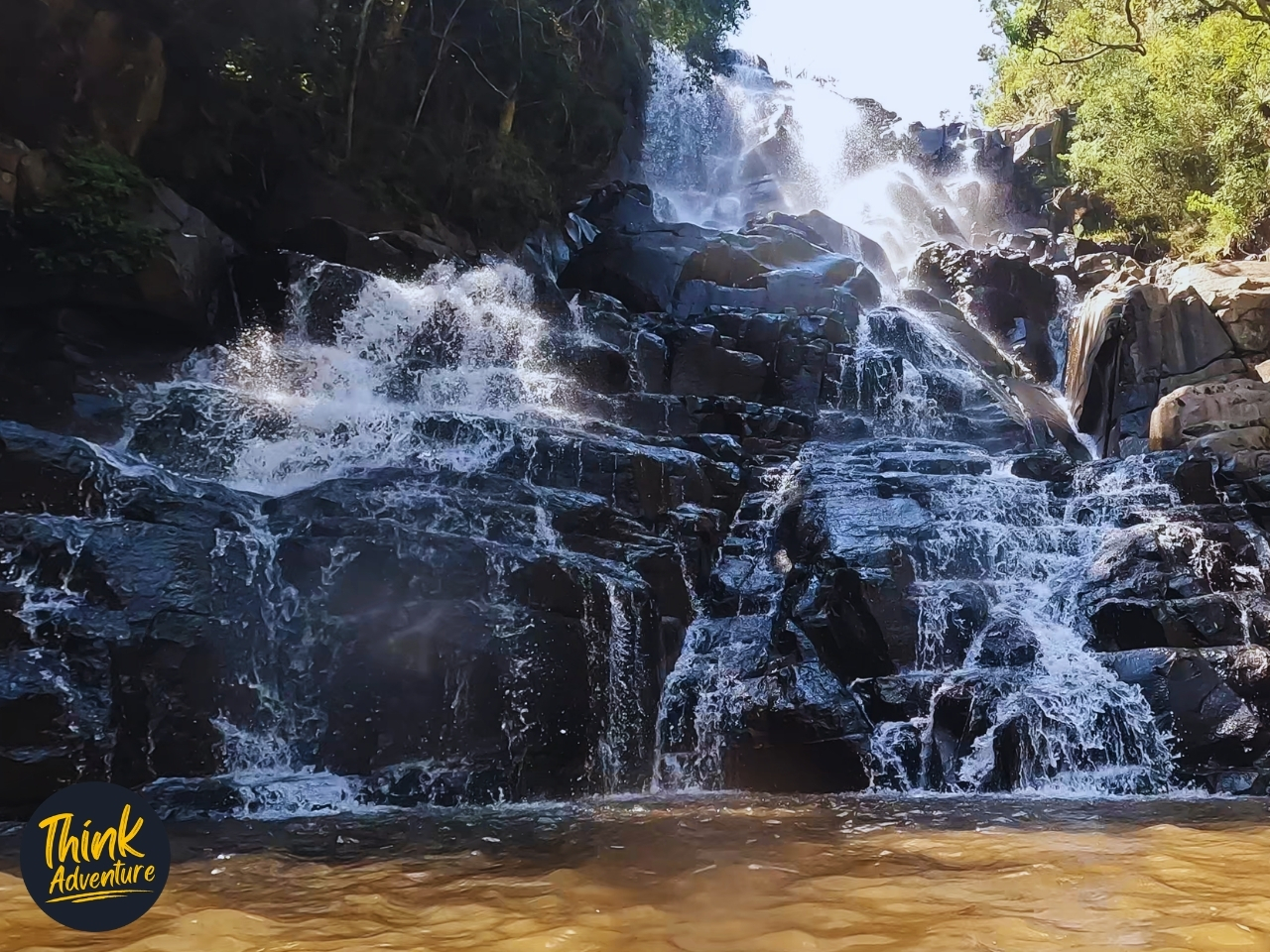 Waterfall cascading over dark rock into a tea-coloured rock pool on the Lynx Loop at Wathaba Hiking Trails, Mpumalanga